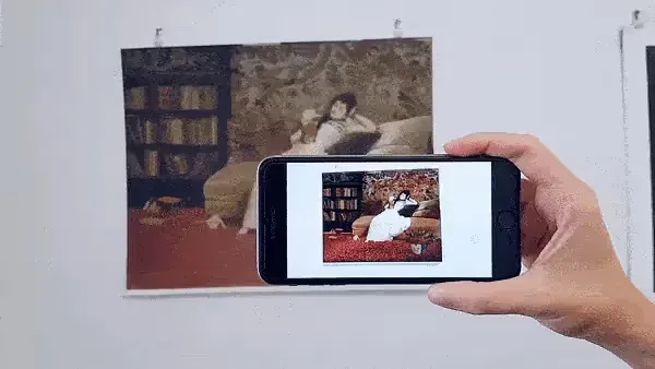 Phone held over a print of a woman reading on a sofa, the screen showing Elizabeth Leister's animated AR version