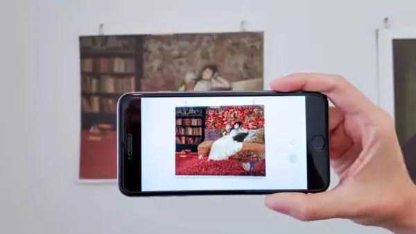 Phone over a print of a woman on a sofa, the AR layer on screen filling the scene with red flowers