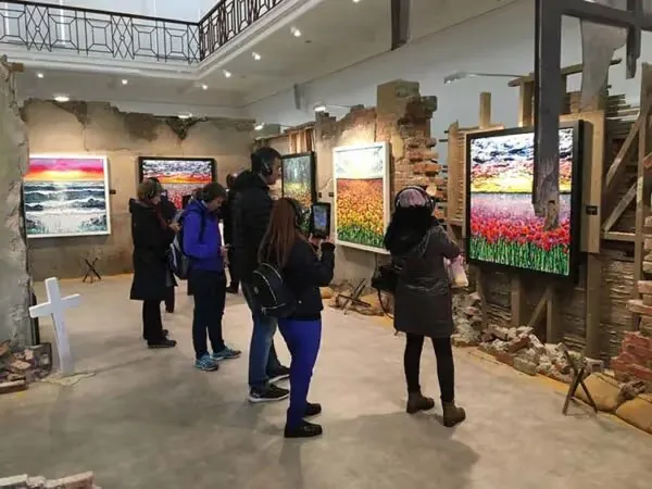 Visitors with headphones and tablets viewing Marc Marot and Scarlett Raven's poppy and seascape paintings in AR