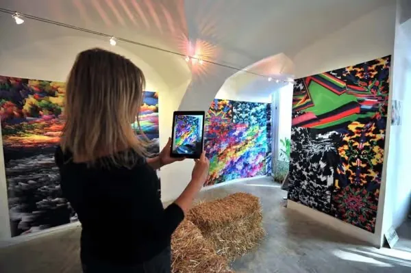 Woman holding a tablet up to vivid abstract digital artworks by Station Rose in a vaulted gallery