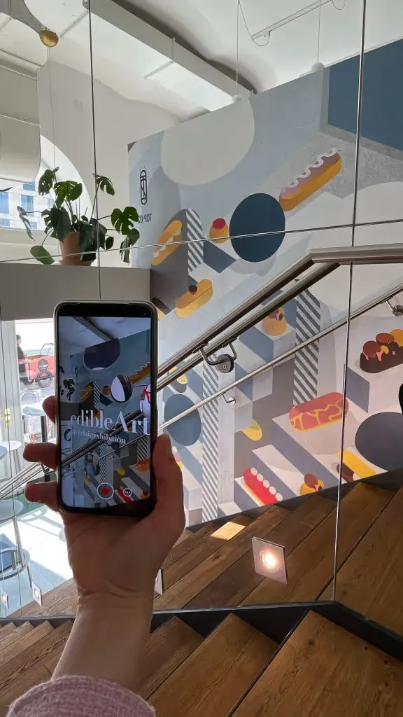 Phone held up to the pastry shop's eclair mural, the screen showing the edible Art AR experience