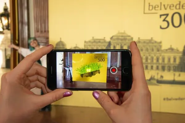 Phone pointed at the Belvedere 300 selfie wall, the screen showing a green AR animation