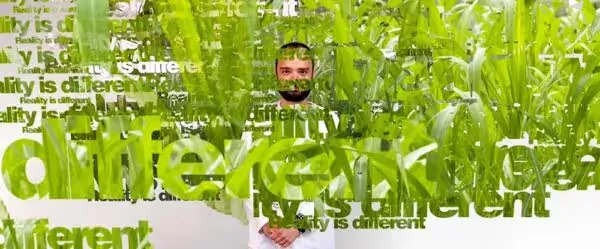 Man surrounded by tall green grass and repeated text reading Reality is different