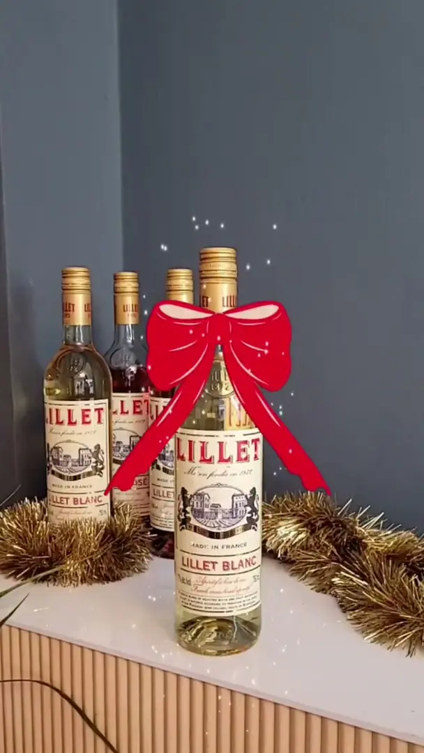 Lillet Blanc bottles on a shelf, a phone showing a red ribbon bow and falling snow around one of them