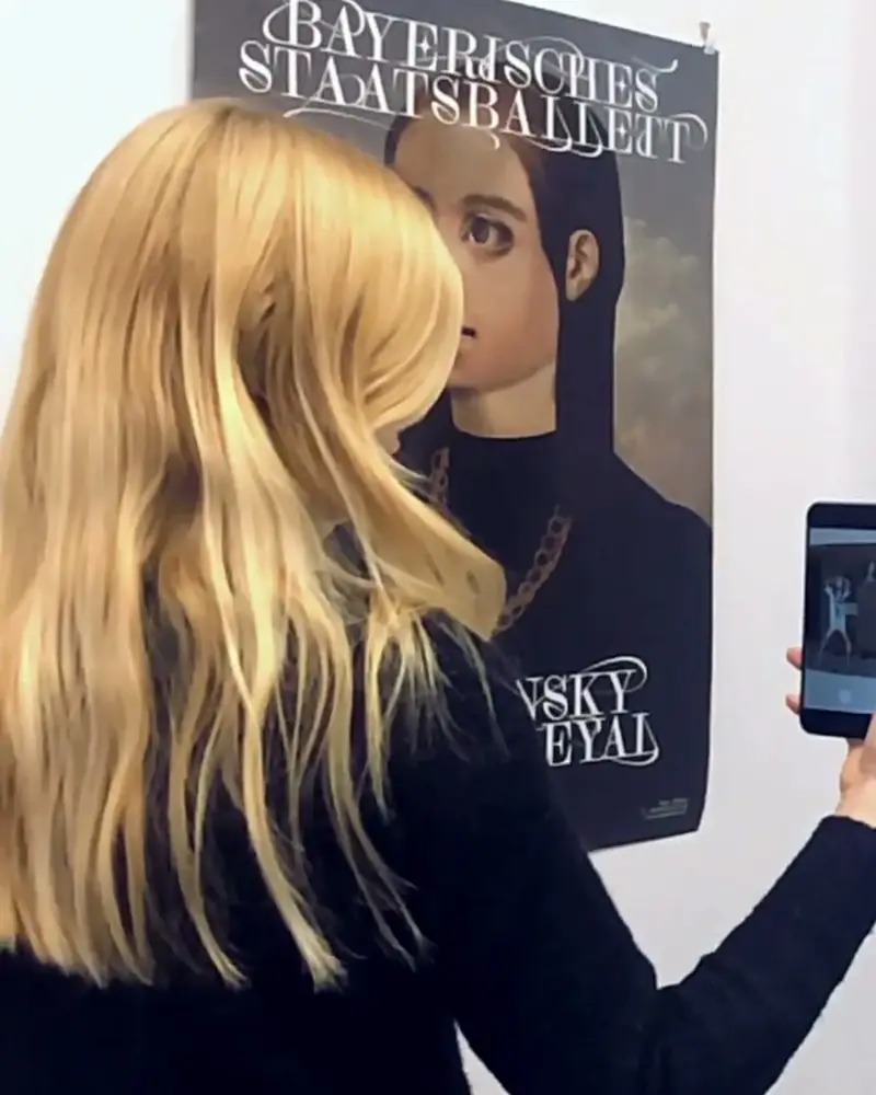 A woman scans an opera poster by Scorpion Dagger for the Bayerische Staatsoper with her phone