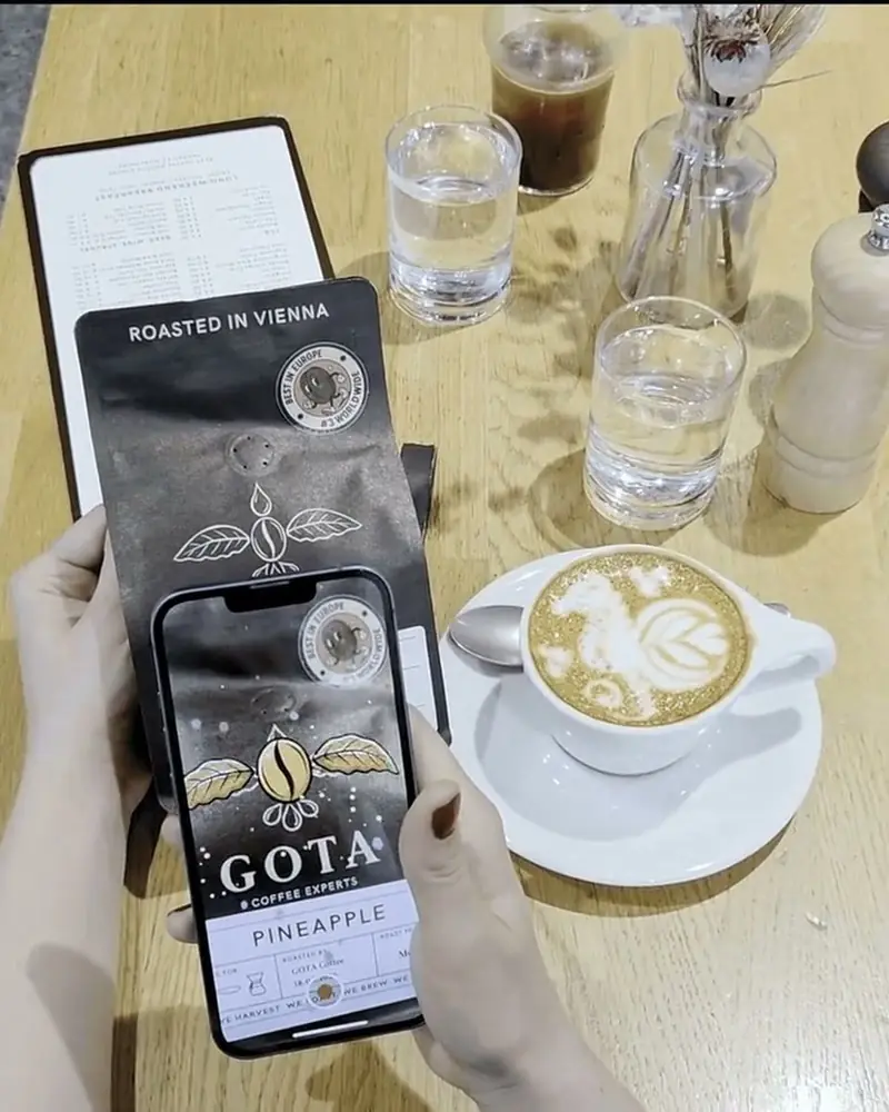 A Gota Coffee bag scanned with a phone at a café table: the pack’s design comes to life on screen