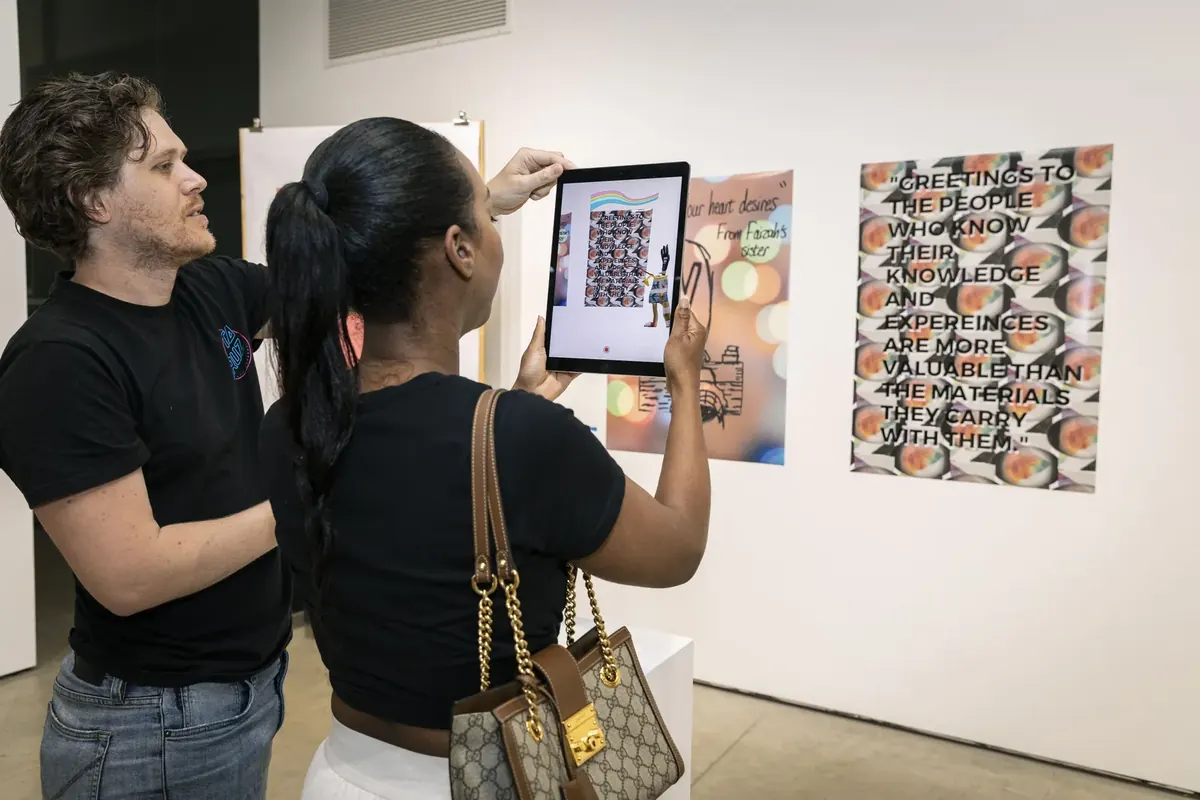 Two visitors scan a student poster with a tablet at a Ricebox Studio exhibition