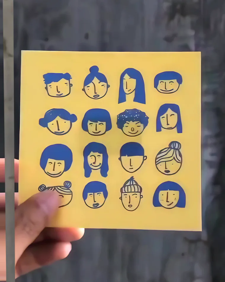 The plain print against a concrete wall: sixteen faces drawn in blue ink on yellow paper