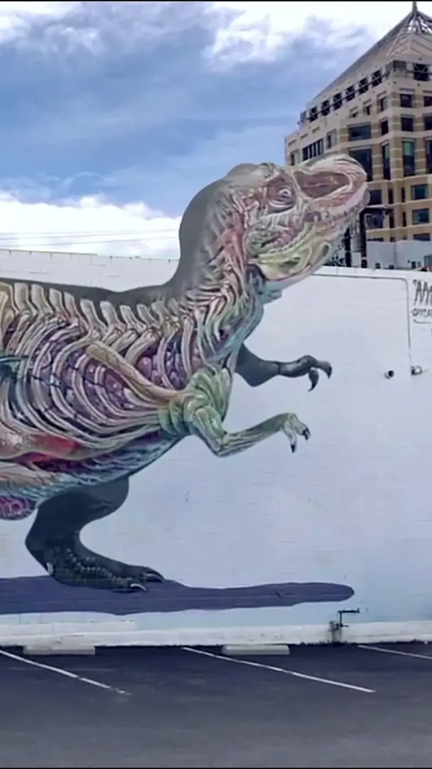A phone held up to the T-Rex mural by Nychos in Oakland, the skeleton coming to life on screen