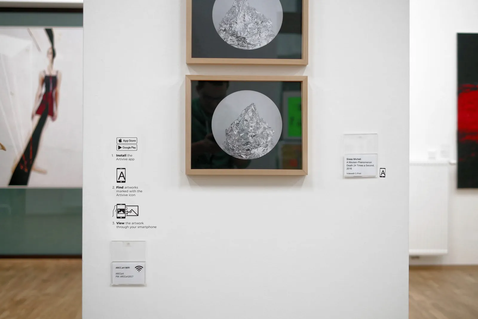 A gallery wall with two framed artworks and the Artivive instruction signs beside them
